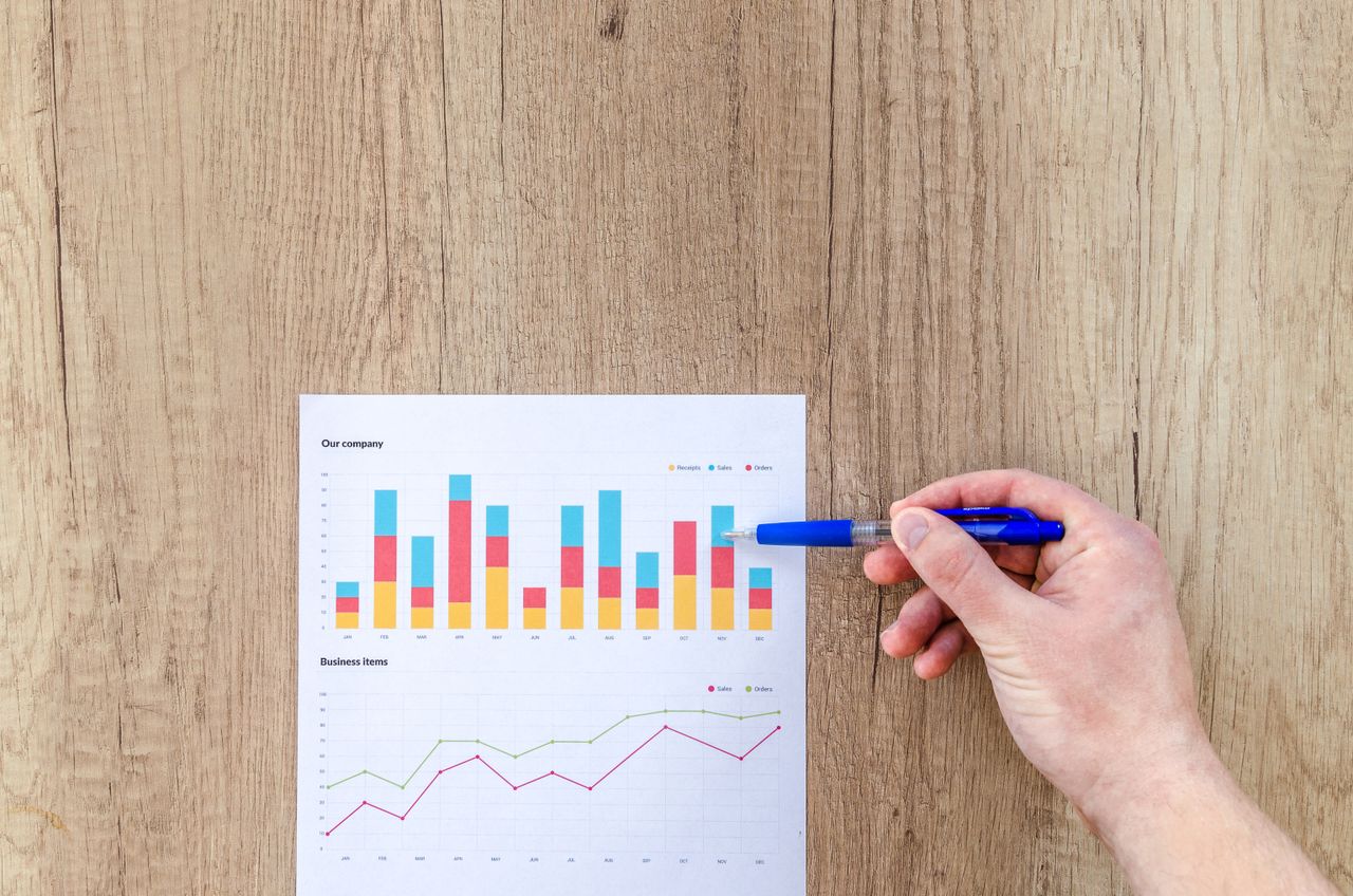 Services-02 A hand points a pen at business graphs on a wooden table, highlighting data analysis.